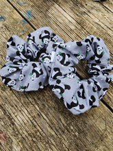 Load image into Gallery viewer, A gray scrunchie with a pattern of black and white pandas and bamboo on it, displayed on a wooden surface.