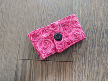 Load image into Gallery viewer, pink drink cozie with rose pattern and black button on a wood surface