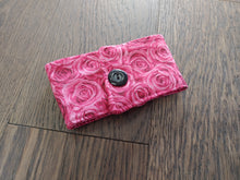 Load image into Gallery viewer, A pink drink cozie with a rose pattern and an acrylic button, placed on a wooden surface.