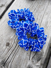 Load image into Gallery viewer, Two blue scrunchies with white lattice patterns, placed on a wooden surface.