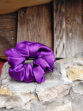 Load image into Gallery viewer, A purple silky scrunchie placed on a stone surface with a wooden background.