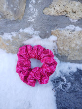 Load image into Gallery viewer, A pink cotton scrunchie with a rose pattern, placed on a textured surface with snowflakes around.