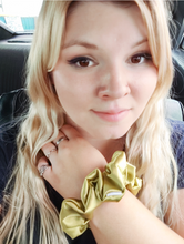 Load image into Gallery viewer, A person showing off a golden satin scrunchie, with a focus on the texture and color of the material.
