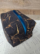 Load image into Gallery viewer, Black and gold patterned pouch with a blue interior 
