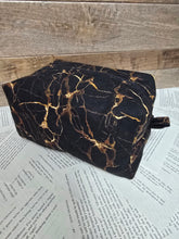 Load image into Gallery viewer, Black and gold marbled object on a textured surface with text
